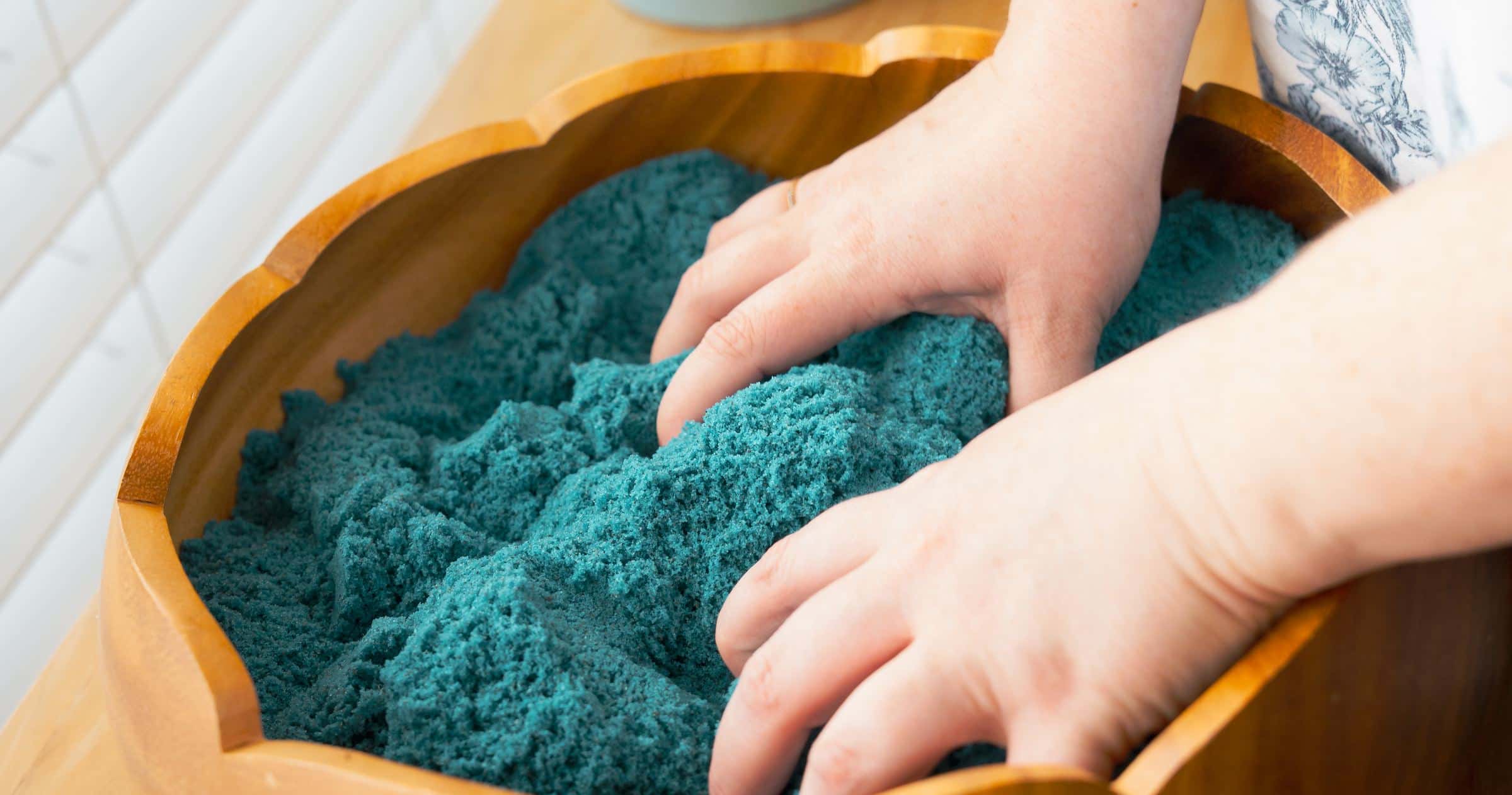 Hands resting in a bowl of teal kinetic sand on a wooden table in the Texarkana Counseling Collective office.